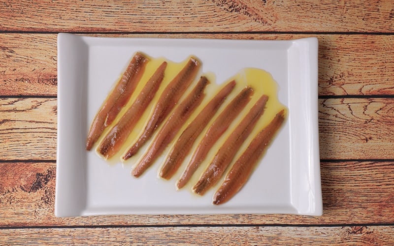 Porción de anchoas de Santoña, anchoas cántabras en placa rectangular blanca sobre mesa de madera